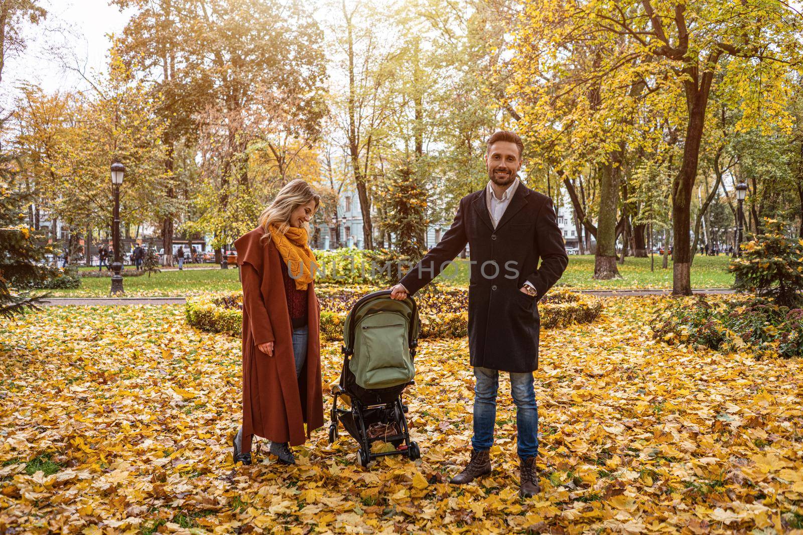 Walking in an autumn park young family with a newborn baby in a stroller. Family outdoors in a golden autumn park. Tinted image. 