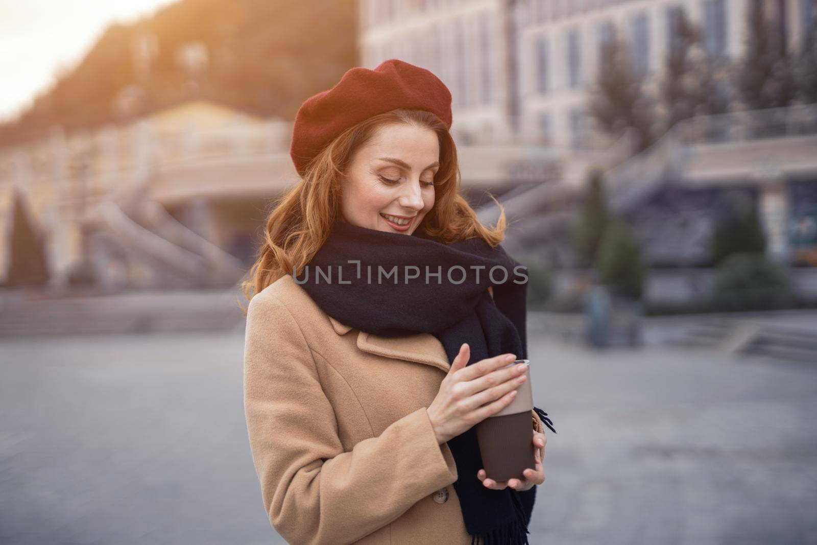 Warming up with cup of coffee on the street female fashion. Portrait of stylish young woman wearing autumn coat and red beret outdoors. Autumn accessories. 