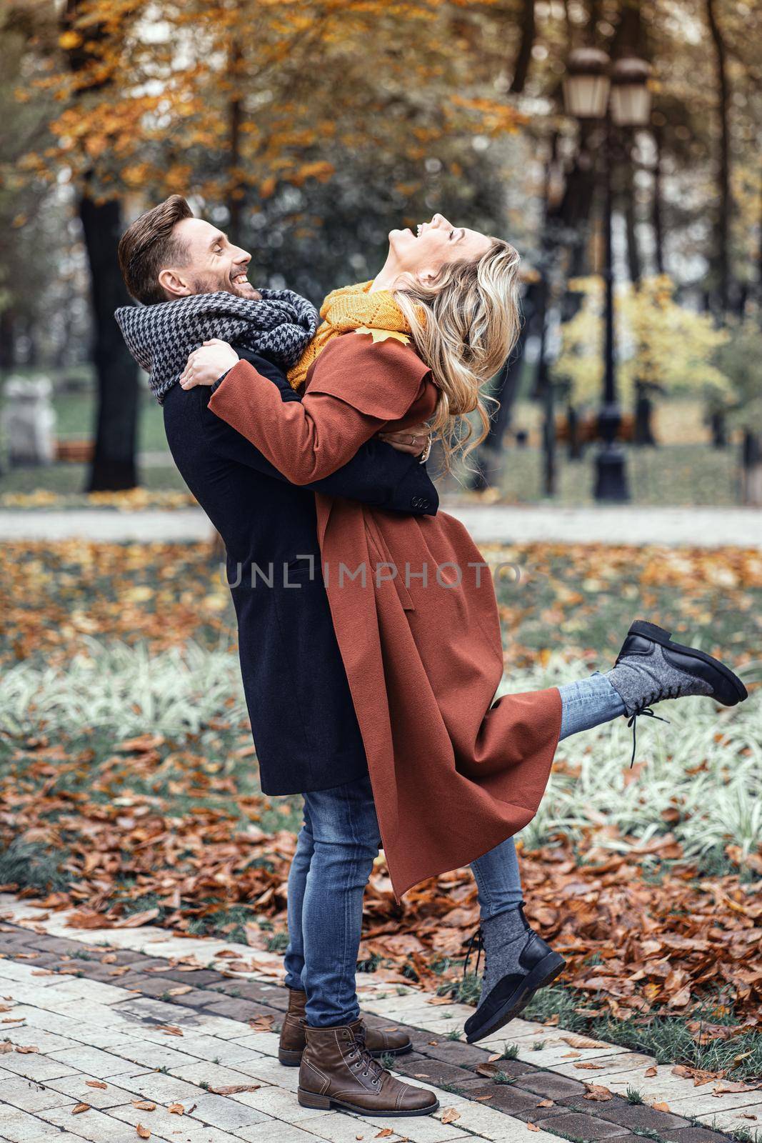 Man lifting a girl hugged laughing in the autumn park with a cute hug. Outdoor shot of a young couple in love having great time having a hug in a autumn park. Close up full length.Tinted image by LipikStockMedia