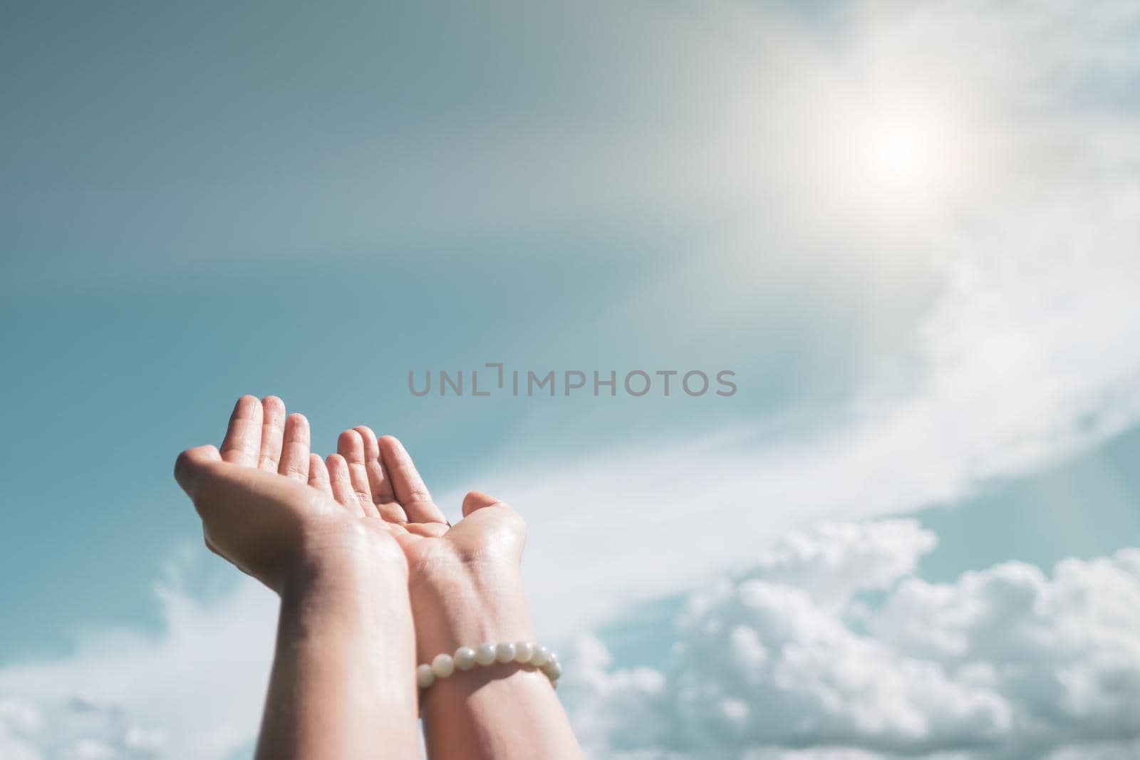 Woman hands place together like praying in front of nature blue sky background.