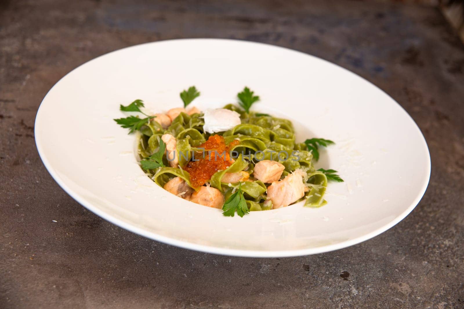 green pasta with salmon and red caviar and greens in a white plate by Pukhovskiy