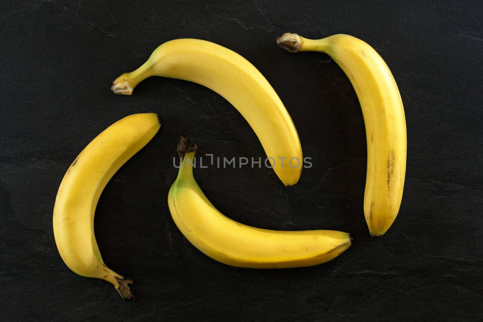 Flat lay photo - 4 bananas on black desk.