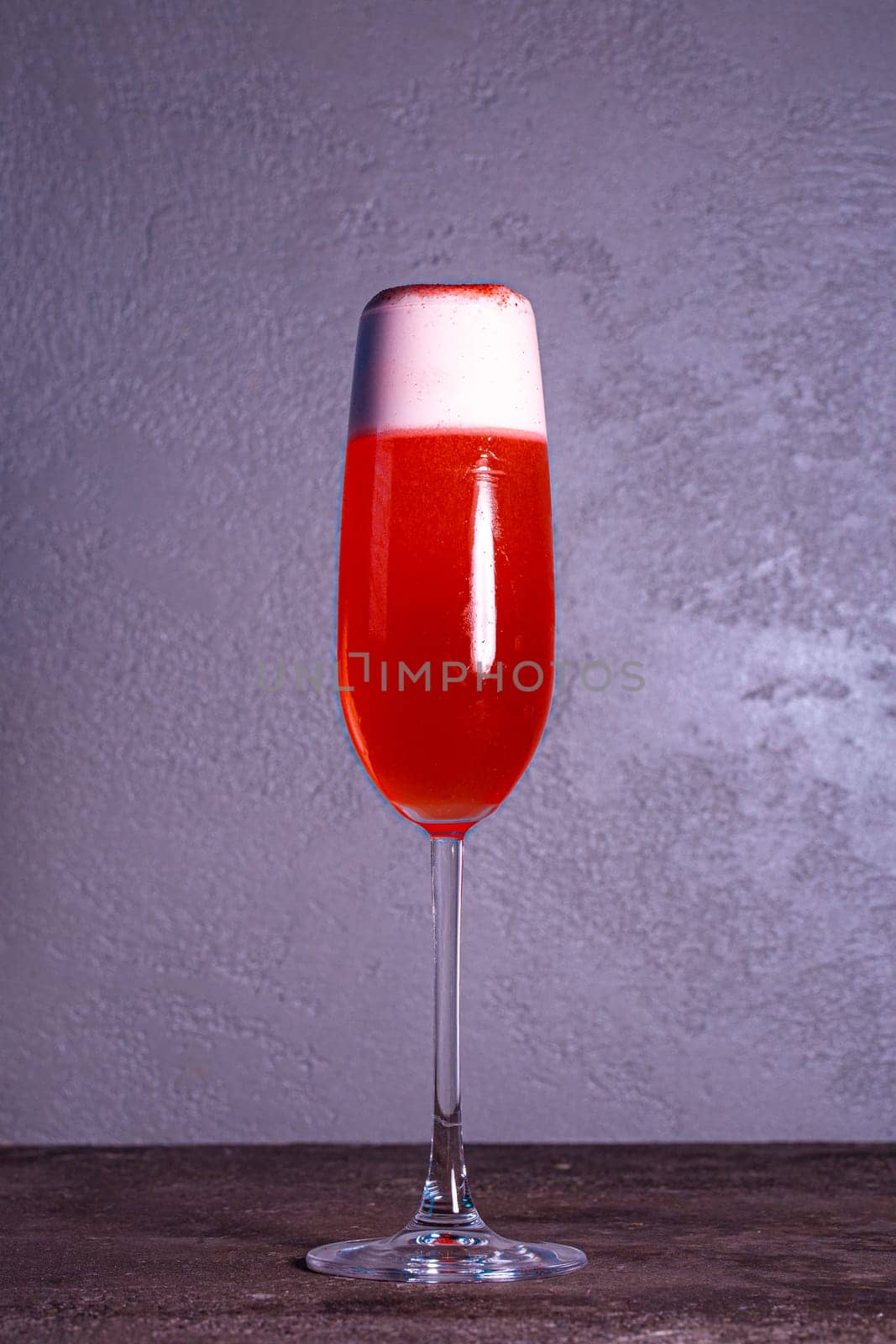 red refreshing cocktail with foam in a glass on a gray background.