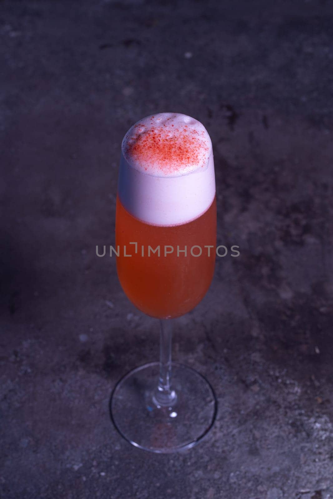 red refreshing cocktail with foam in a glass on a gray background.