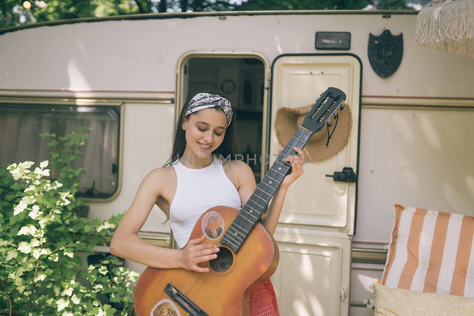 Happy hippie girl are having a good time with playing on guitar in camper trailer. Holiday, vacation, trip concept.High quality photo