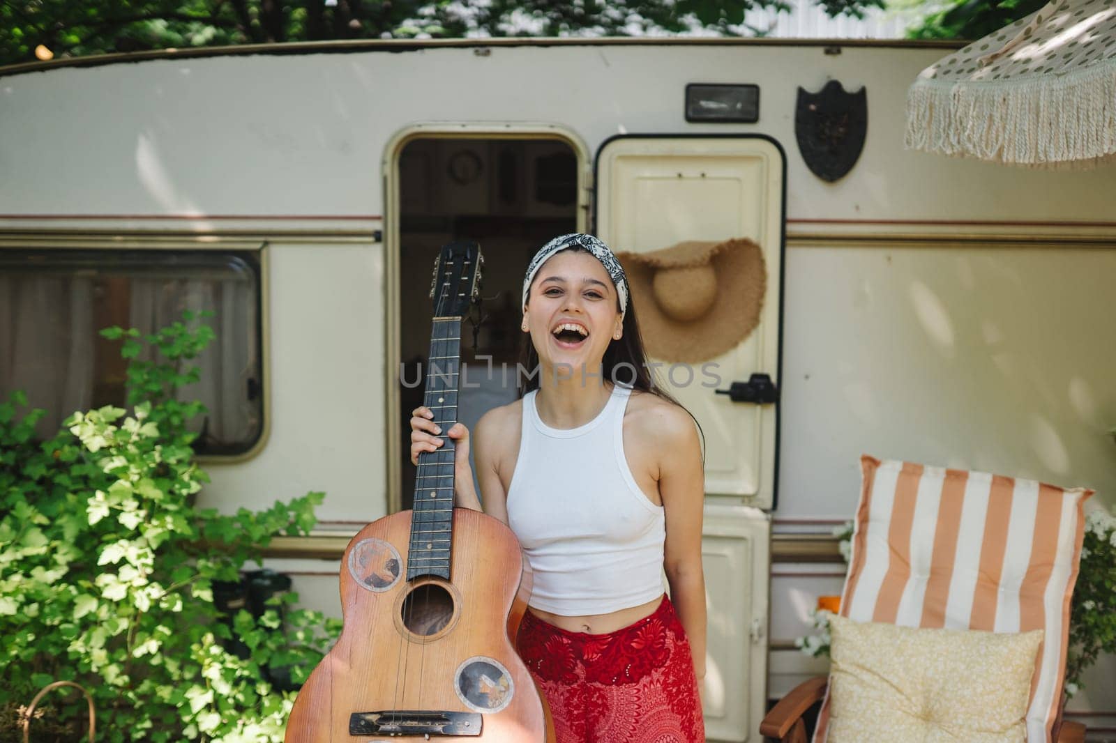 Happy hippie girl are having a good time with playing on guitar in camper trailer. Holiday, vacation, trip concept.High quality photo