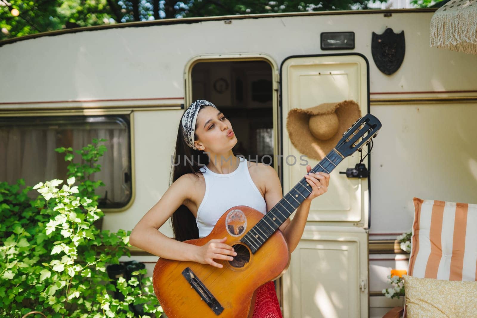 Happy hippie girl are having a good time with playing on guitar in camper trailer. Holiday, vacation, trip concept.High quality photo