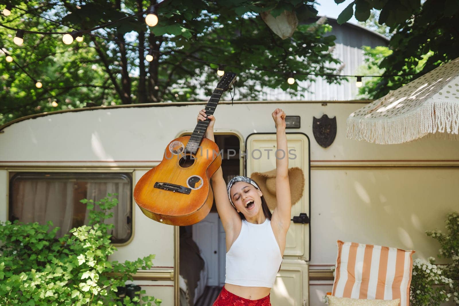 Happy hippie girl are having a good time with playing on guitar in camper trailer. Holiday, vacation, trip concept.High quality photo