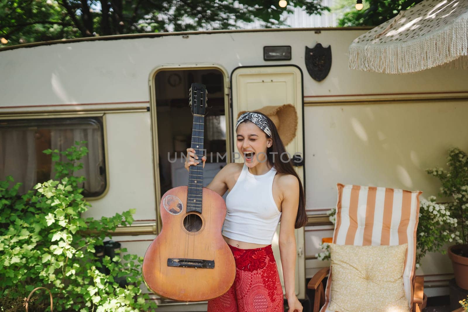 Happy hippie girl are having a good time with playing on guitar in camper trailer. Holiday, vacation, trip concept.High quality photo