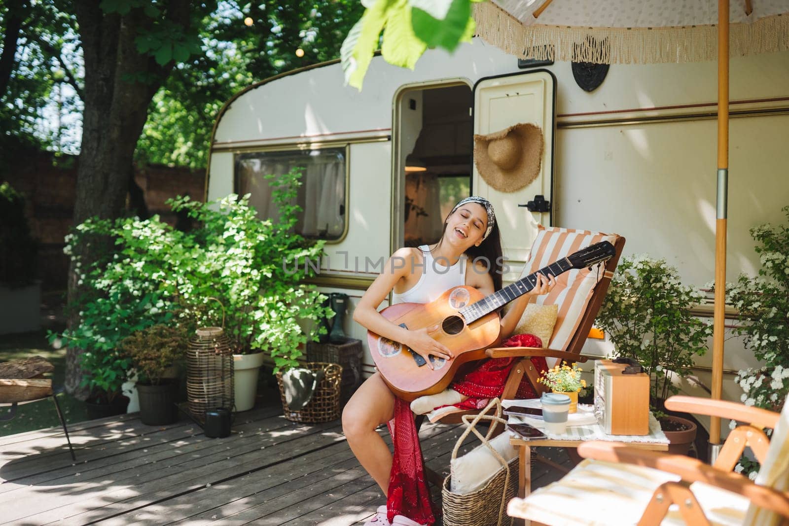 Happy hippie girl are having a good time with playing on guitar in camper trailer. Holiday, vacation, trip concept.High quality photo