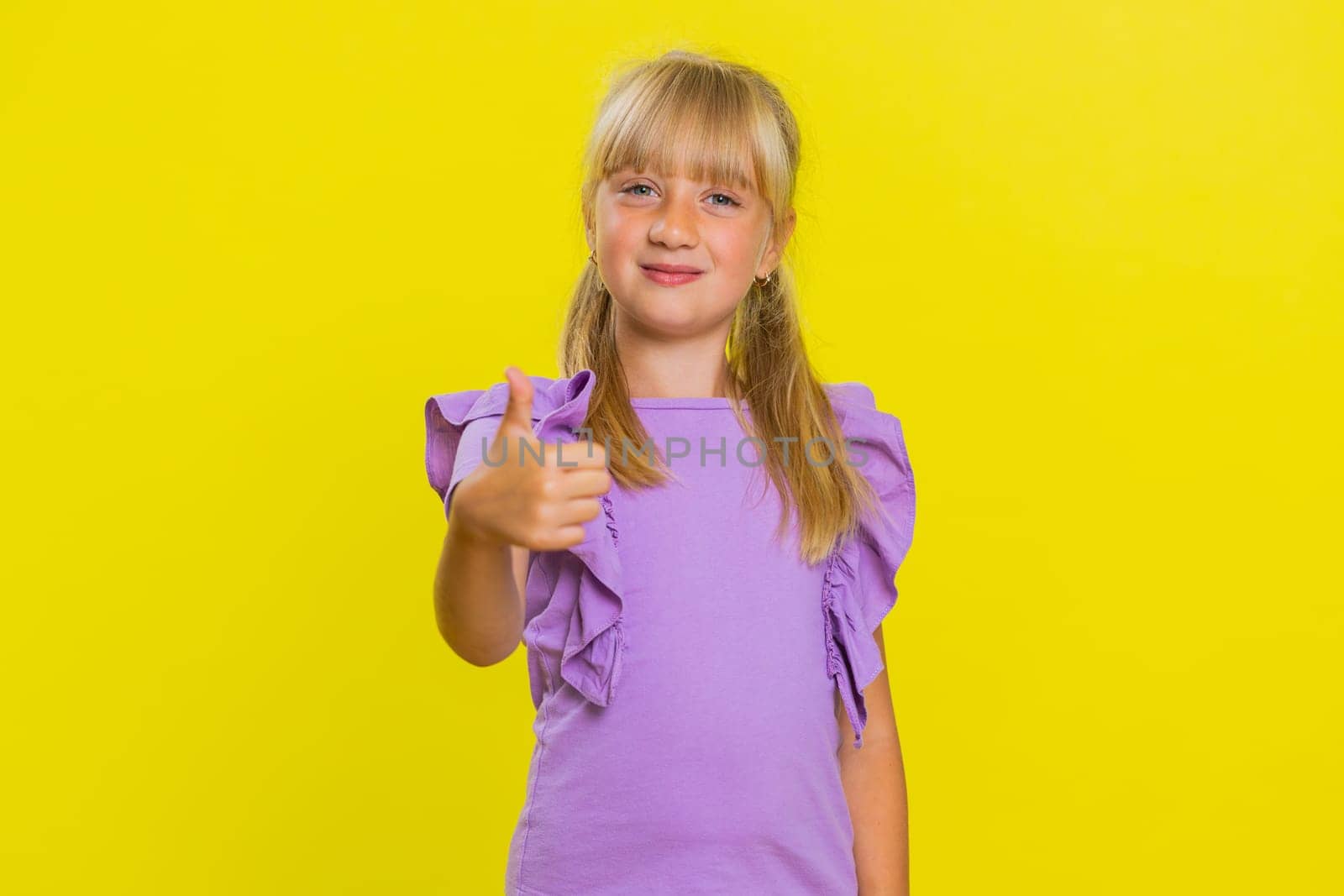 Like. Happy young preteen child girl kid looking approvingly at camera showing thumbs up, like sign positive something good, positive feedback great news. Children isolated on studio yellow background