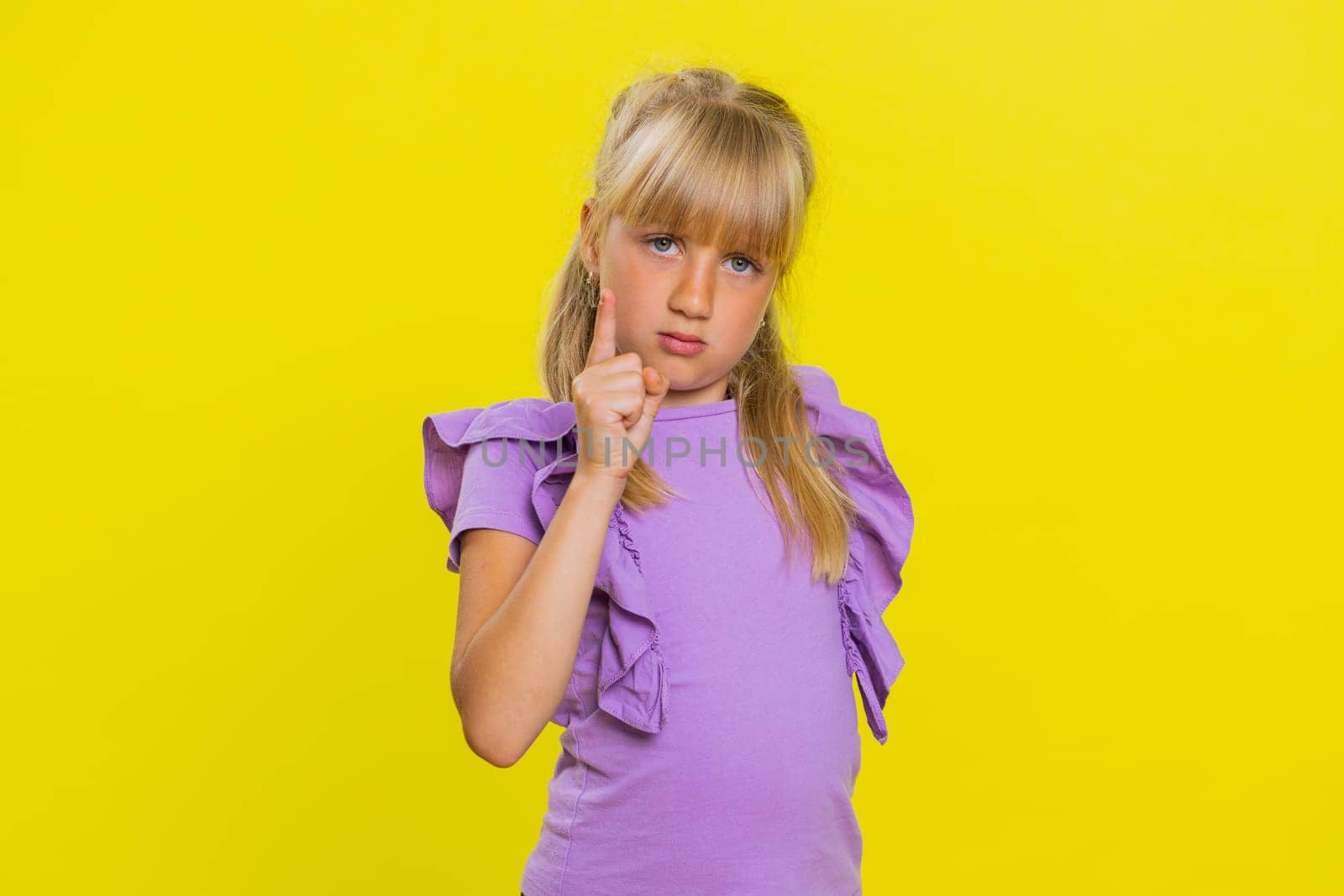 Quarrel. Displeased young cute blonde school girl gesturing hands with irritation and displeasure, blaming scolding for failure, asking why this happened. Preteen female child kid on yellow background