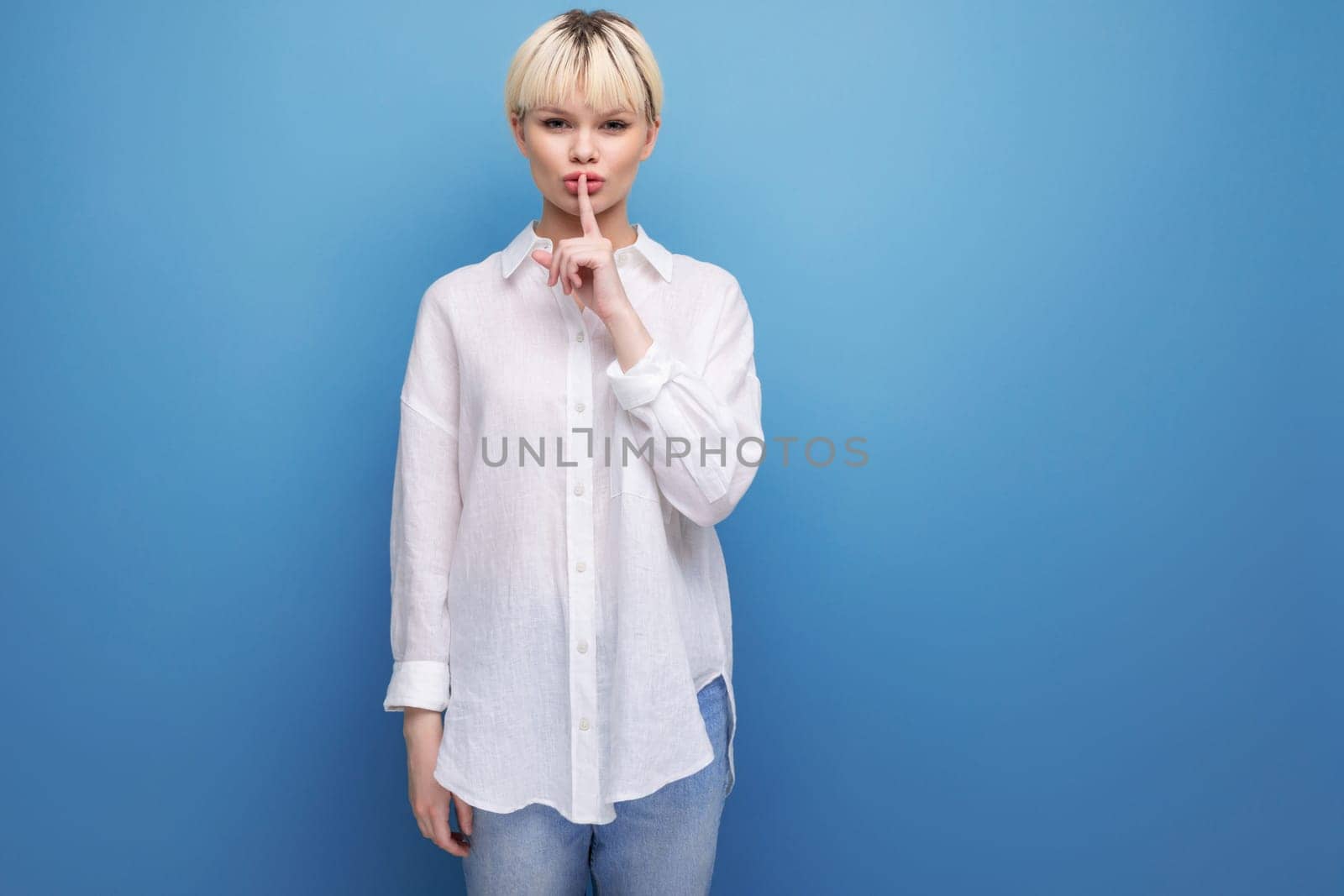 young calm pretty blonde businesswoman in a white shirt keeps a secret on the background with copy space. people lifestyle concept.