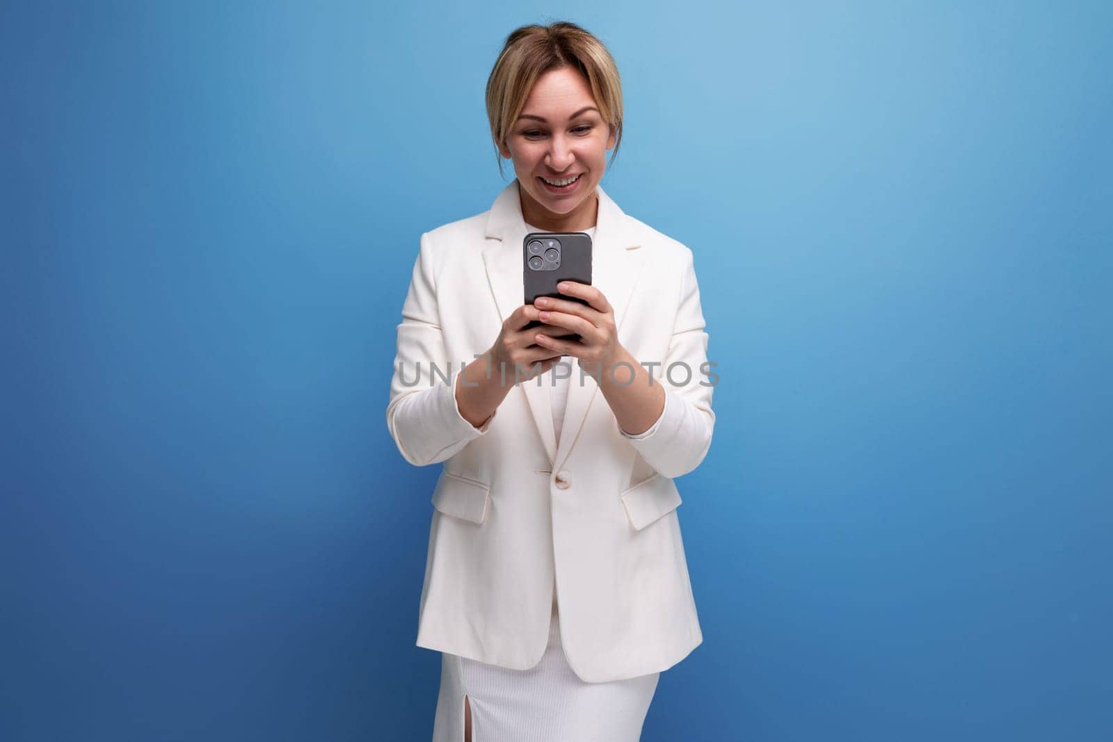 dreamy young caucasian blond lady in an elegant look is typing a message on the phone.
