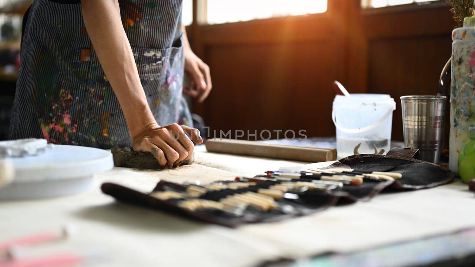 Pottery artist in apron kneading piece of raw clay on wooden table. Handicraft, creativity, hobby and activity concept.