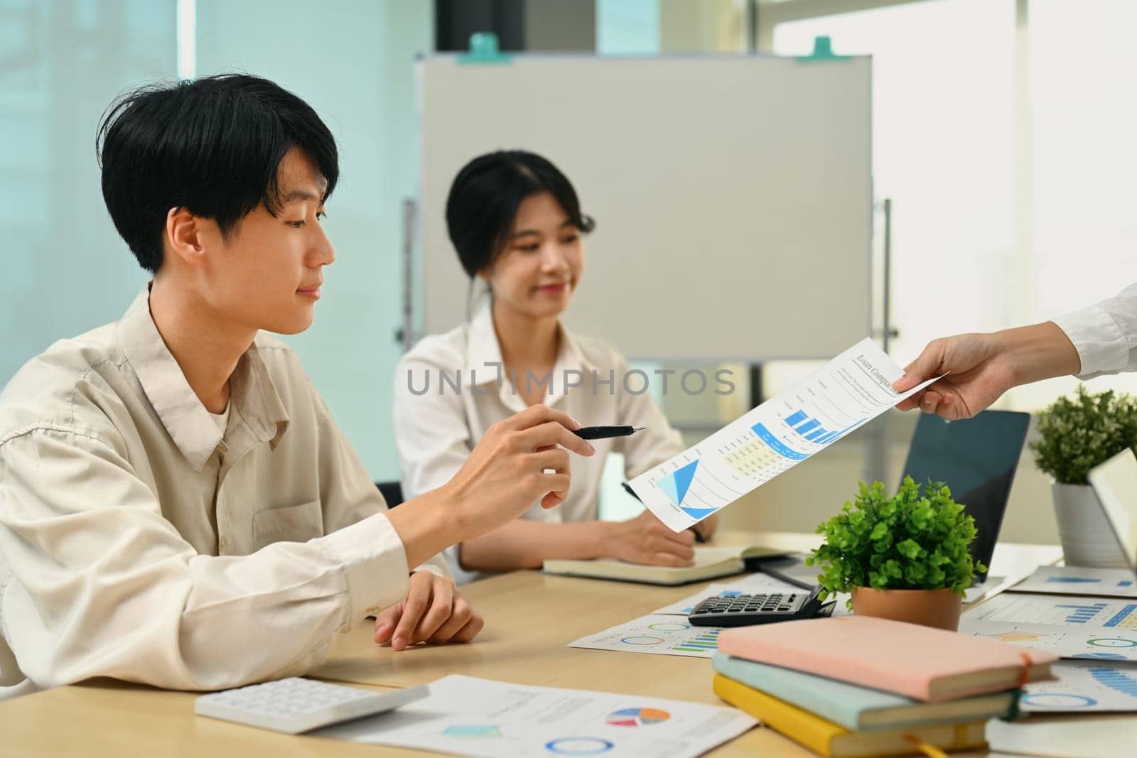 Asian male employee economist analyzing sales statistics document with colleagues at meeting.