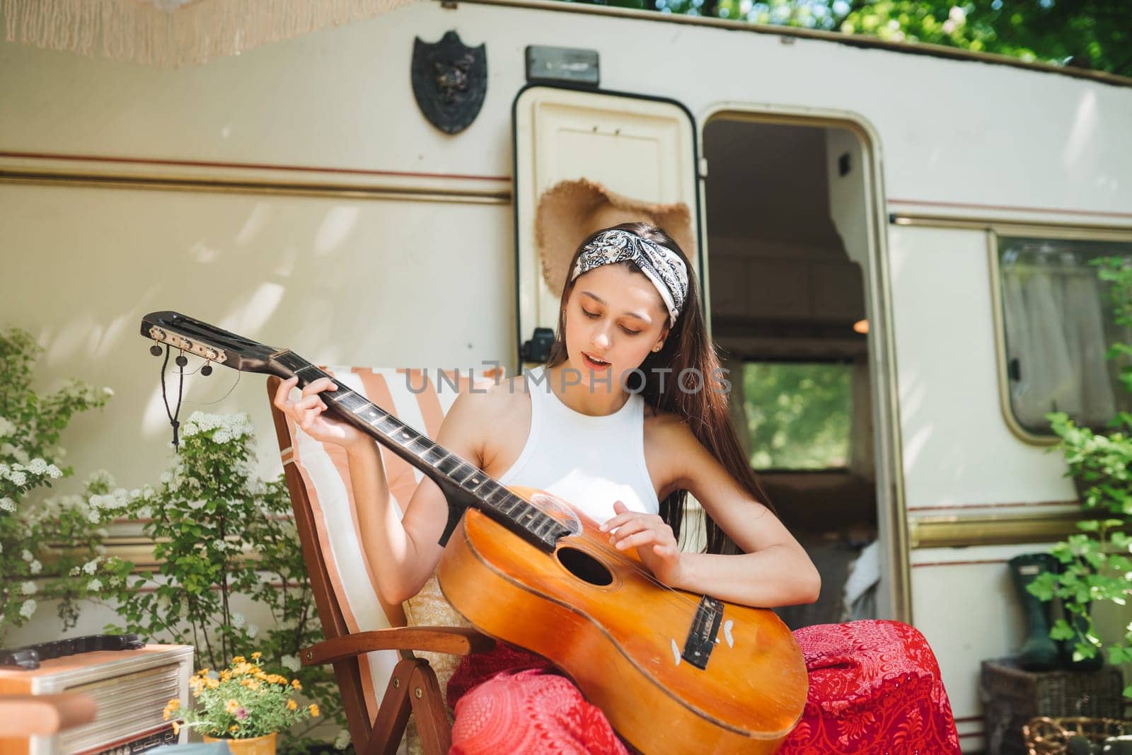 Happy hippie girl are having a good time with playing on guitar in camper trailer. Holiday, vacation, trip concept.High quality photo