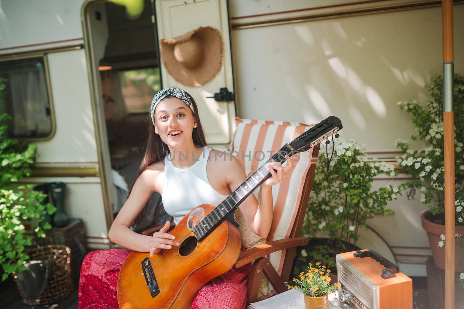 Happy hippie girl are having a good time with playing on guitar in camper trailer. Holiday, vacation, trip concept.High quality photo