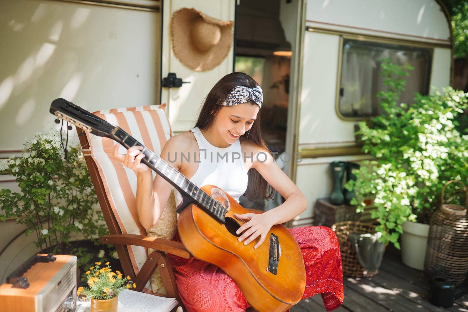 Happy hippie girl are having a good time with playing on guitar in camper trailer. Holiday, vacation, trip concept.High quality photo