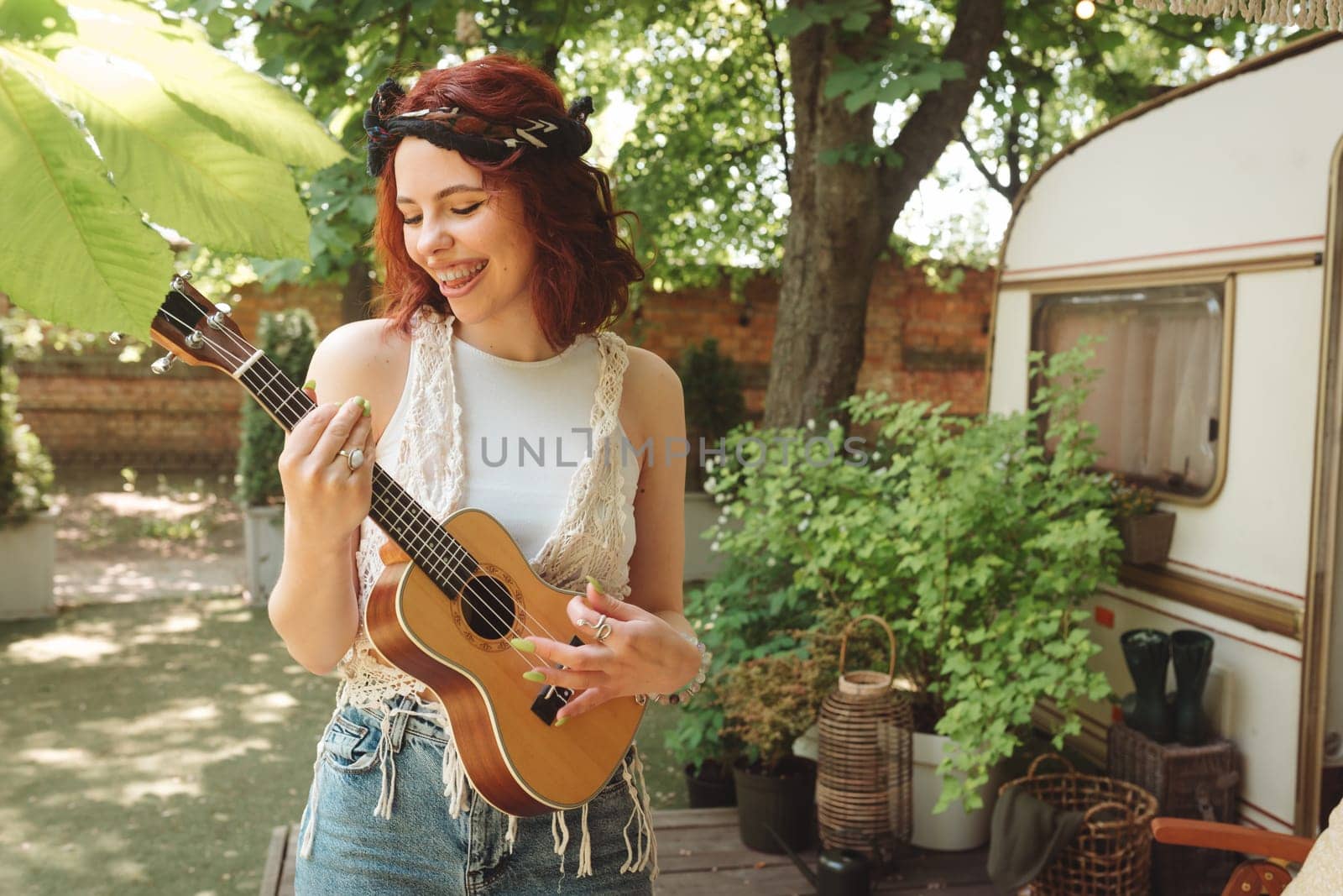 Happy hippie girl are having a good time with playing on guitar in camper trailer. Holiday, vacation, trip concept.High quality photo