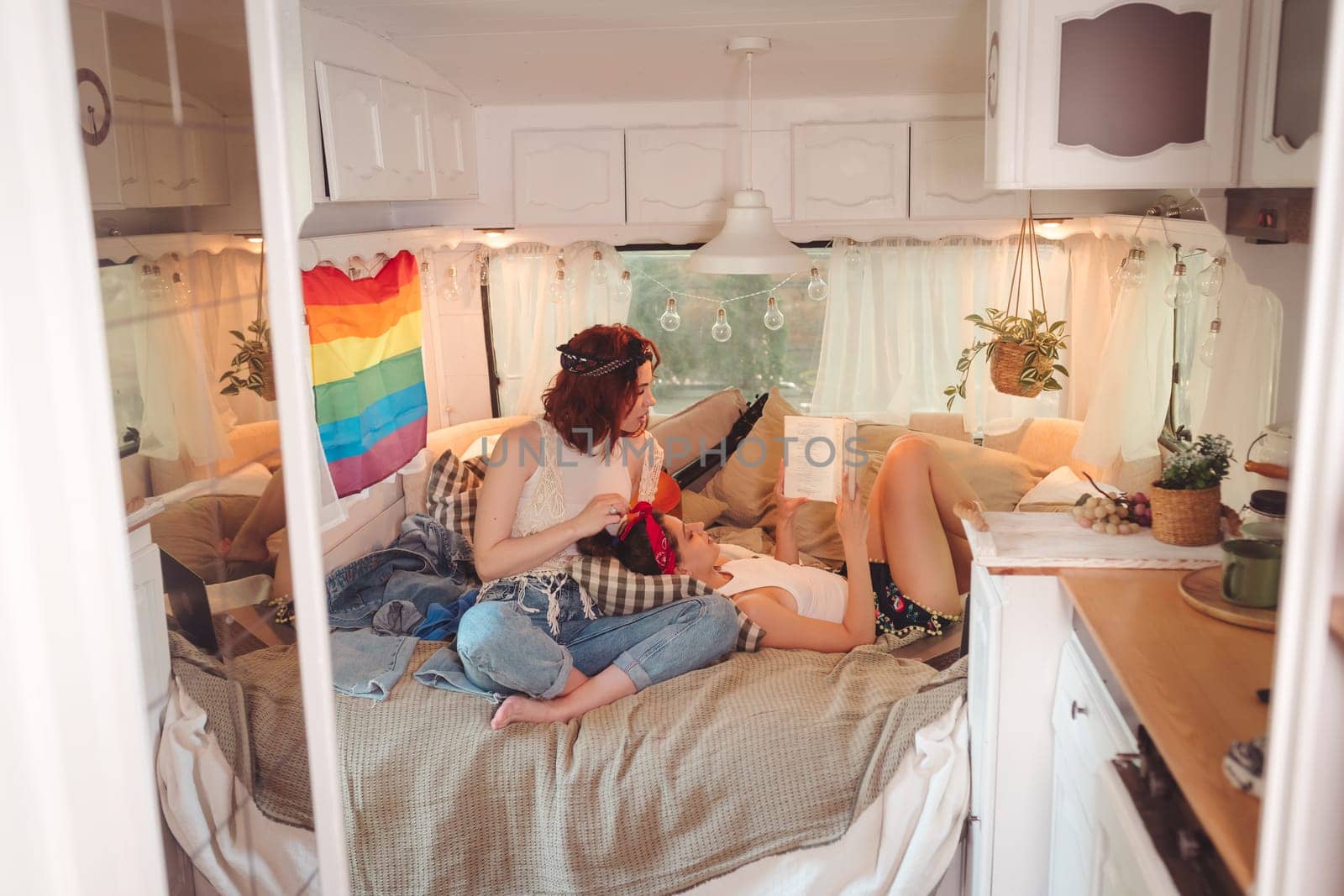 Portrait of a cute lesbian couple. Two girls spend time tenderly together in a camper trailer with LGBT flag on the wall. Love and attitude. LGBT concept. High quality photo