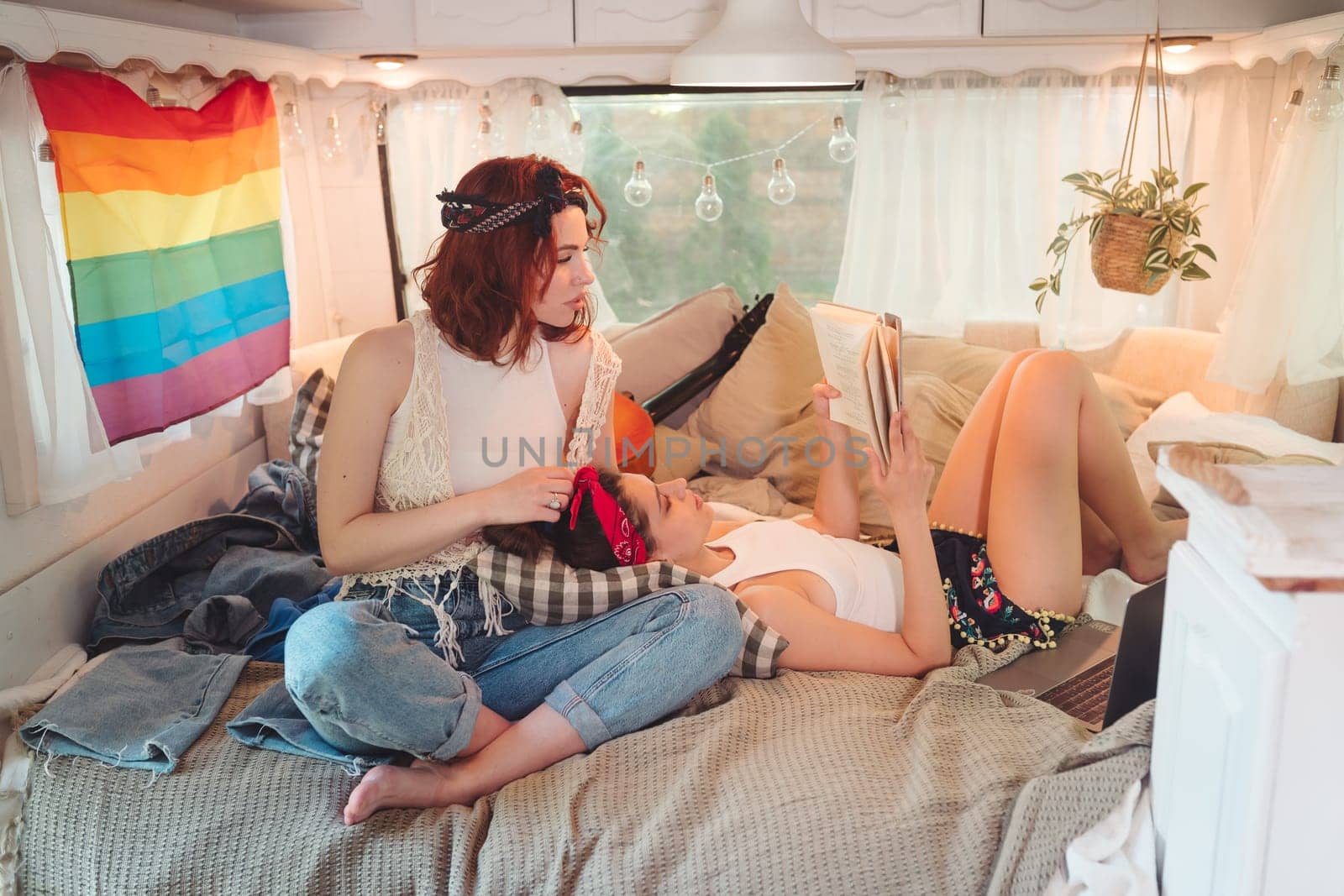 Portrait of a cute lesbian couple. Two girls spend time tenderly together in a camper trailer with LGBT flag on the wall. Love and attitude. LGBT concept. High quality photo