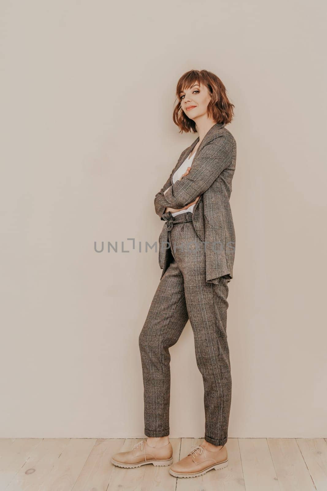 Brunette suit wall. Business woman in a beige suit posing on a beige background. Full length studio portrait