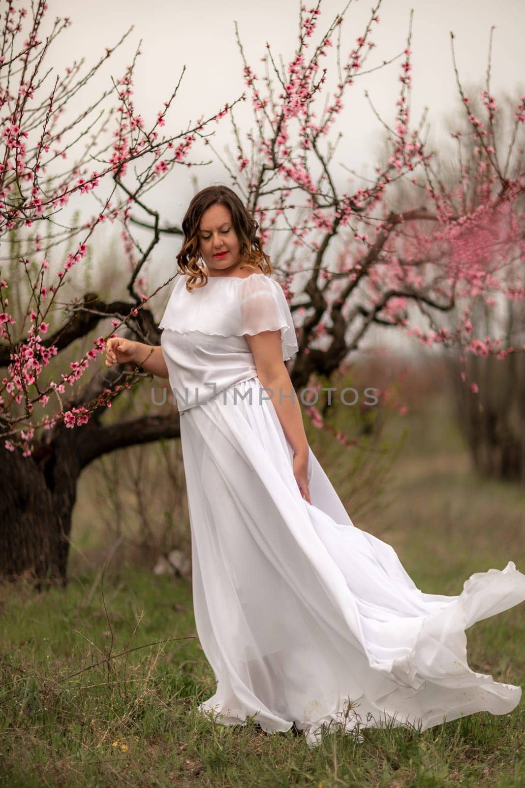 Woman peach blossom. Happy woman in white dress walking in the garden of blossoming peach trees in spring.