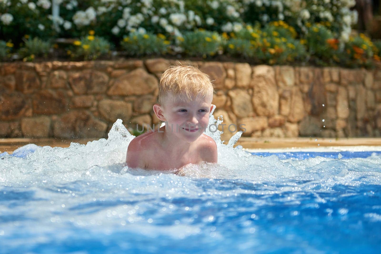 Young boy kid child eight years old splashing in swimming pool having fun leisure activity. Boy happy swimming in a pool. Activities on the pool, children swimming and playing in water, happiness and summertime