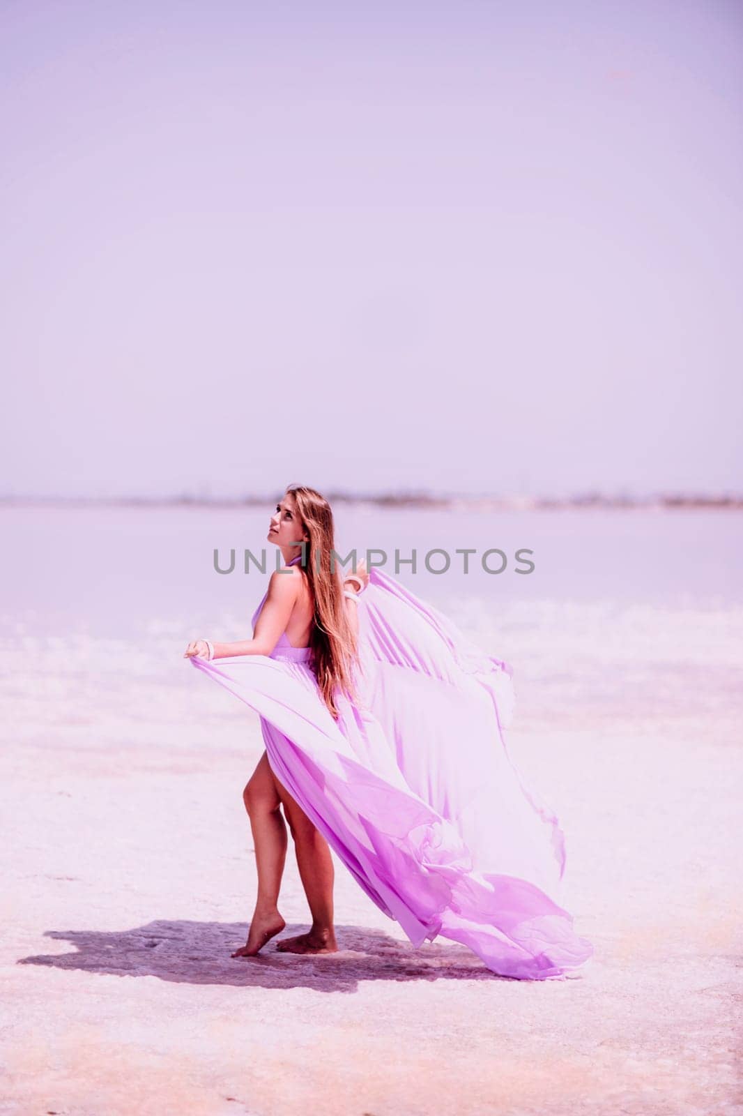 Woman pink salt lake. Against the backdrop of a pink salt lake, a woman in a long pink dress takes a leisurely stroll along the white, salty shore, capturing a wanderlust moment