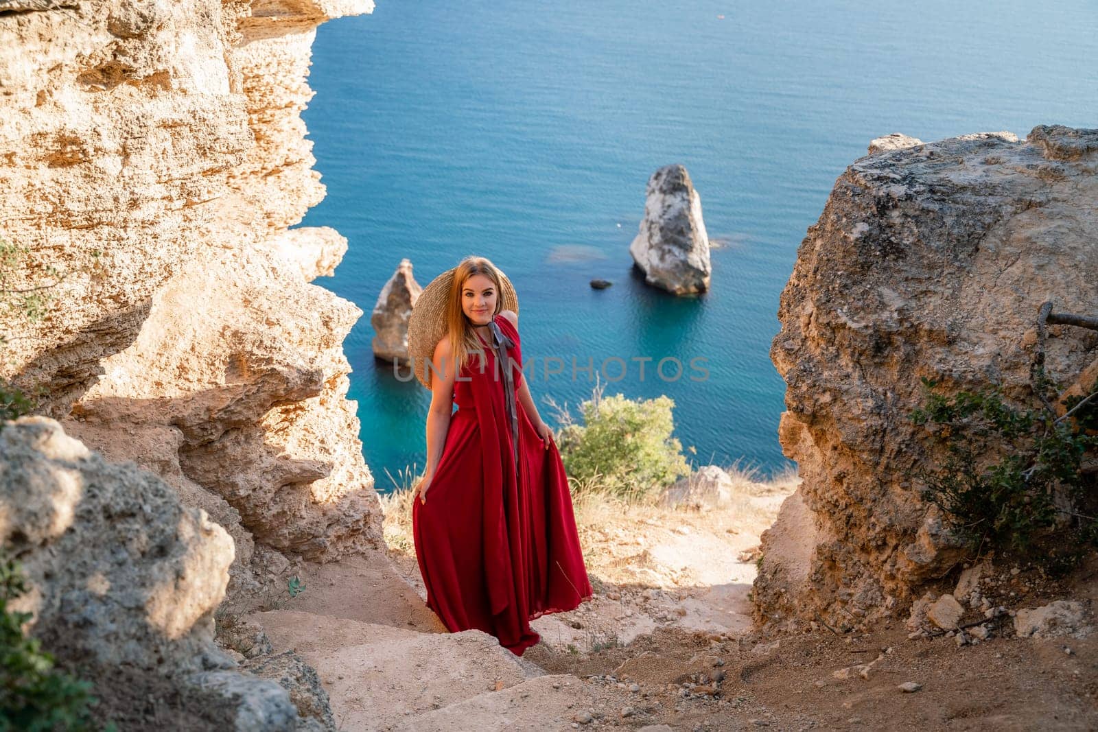 A woman in a red flying dress fluttering in the wind, against the backdrop of the sea