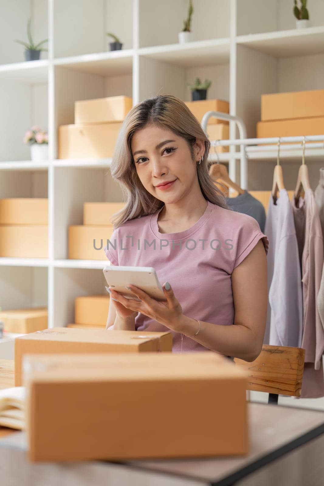 Asian woman entrepreneur beautiful sell clothes online with laptop and product order calculator in office. Online store parcels.