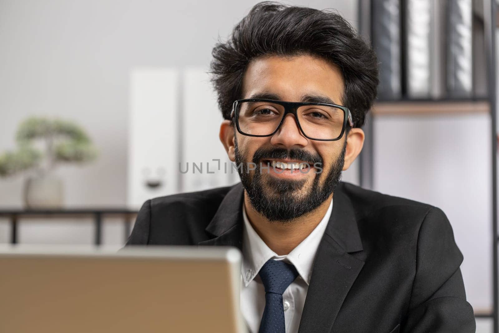 Close-up portrait indian bearded businessman face freelancer at home office workplace working on laptop computer. Manager freelancer indian man works on notebook send messages makes online purchases