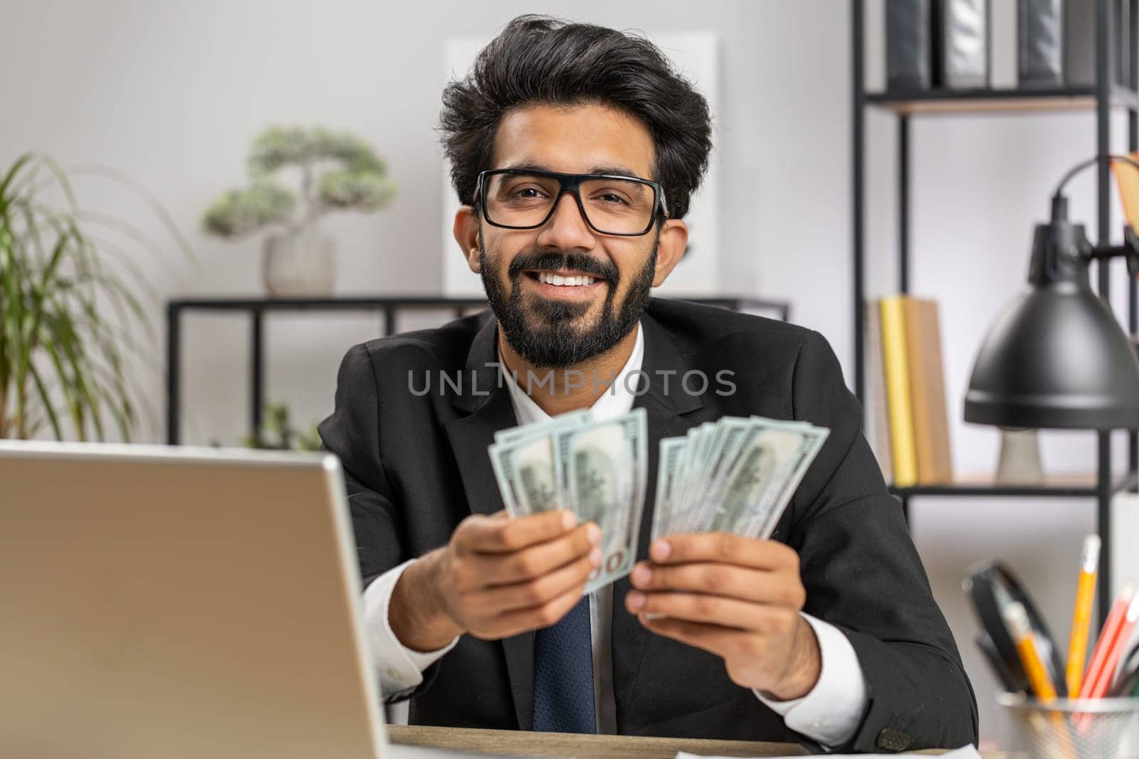 Rich indian businessman working on laptop pc counting money cash, calculate earnings income profit at home office workplace. Professional manager freelancer man. Business people. Employment occupation