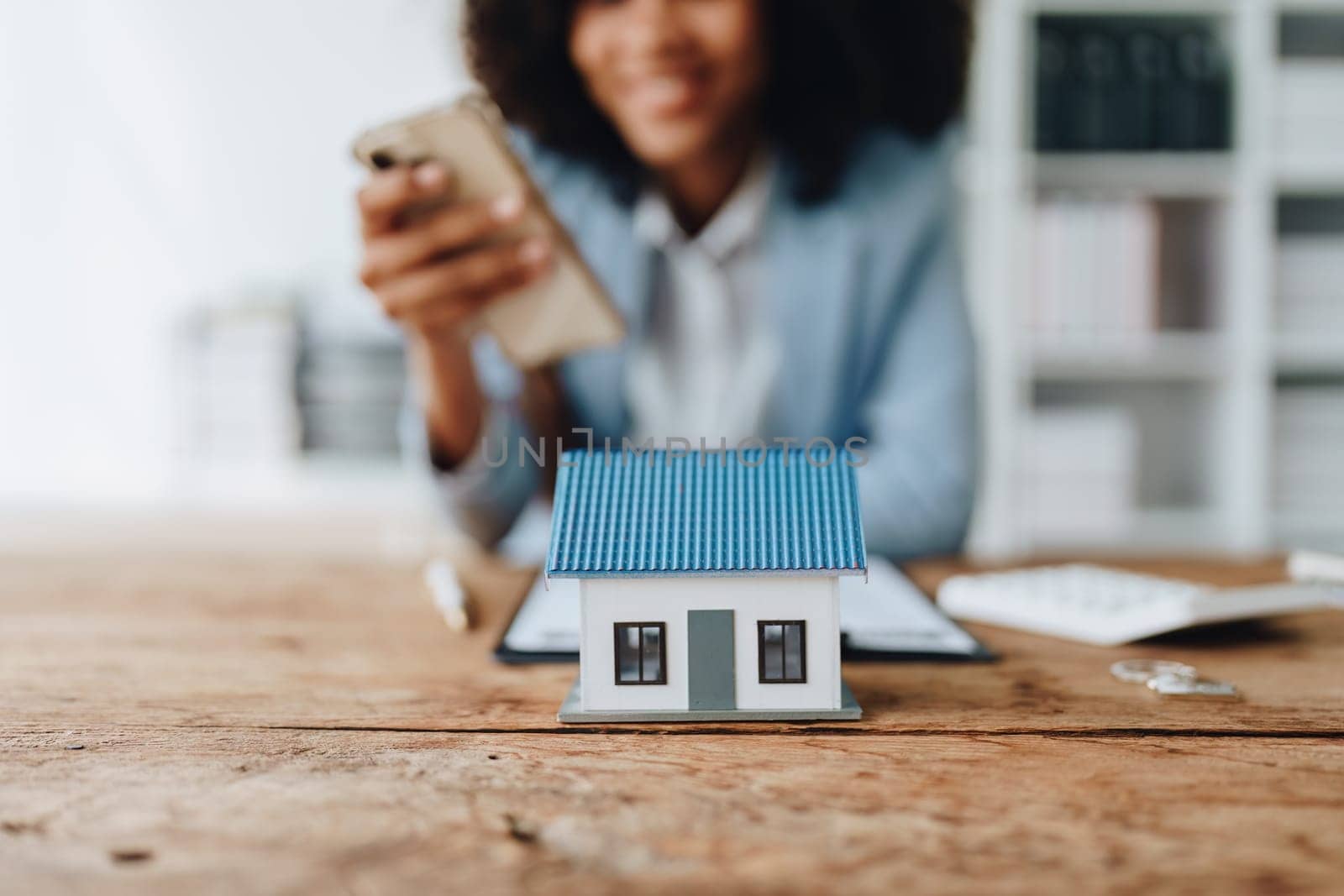 Real estate agent, African American businesswoman Africans use smartphone and calculators to offer mortgages to their clients. Home mortgage and insurance finance concepts by Manastrong