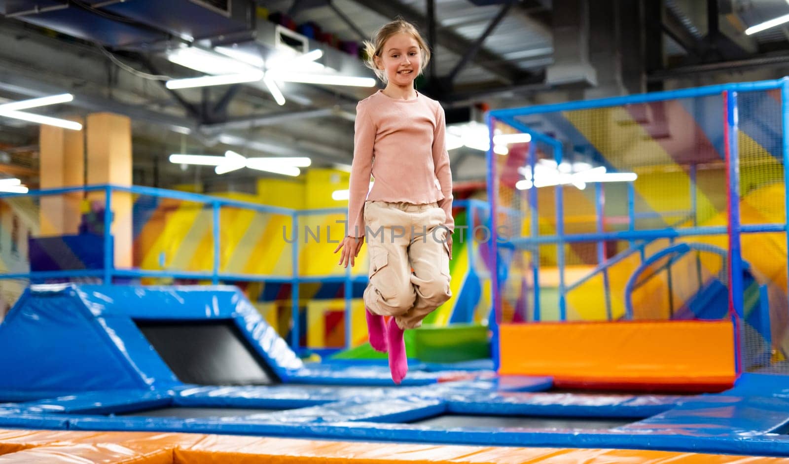 Pretty girl kid jumping on colorful trampoline at playground park and smiling. Beautiful preteen child during active entertaiments