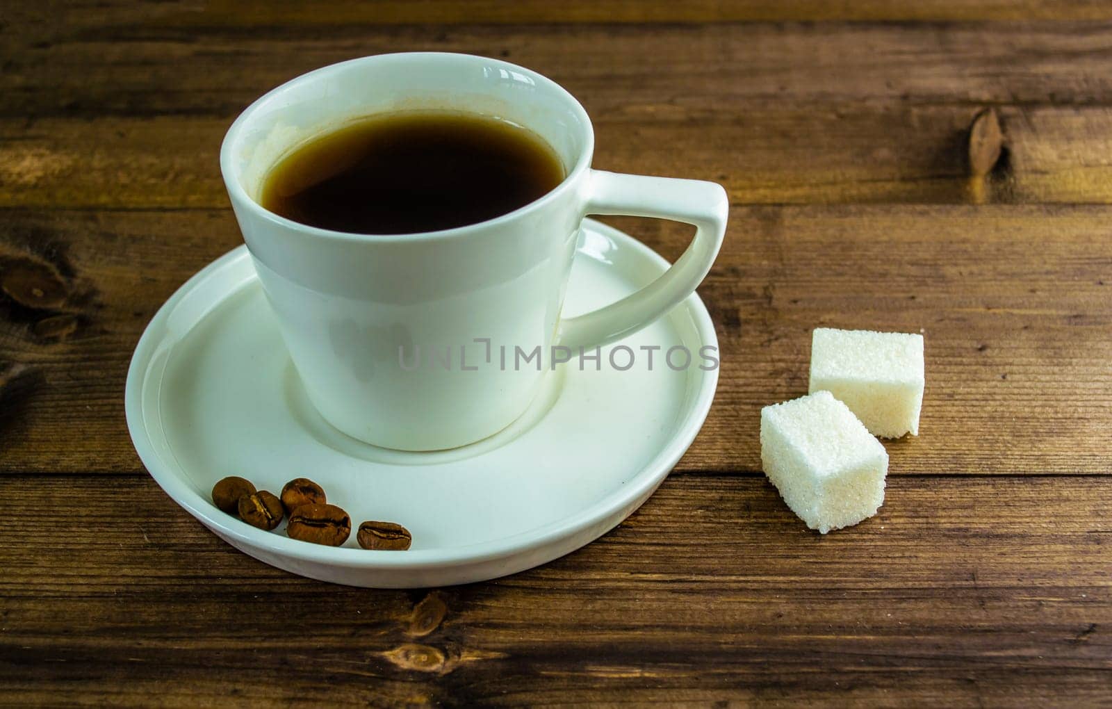 Coffee in a cup, coffee grains and sugar on the table. Coffee in a cup with a saucer, coffee grains and sugar in cubes on a wooden table.