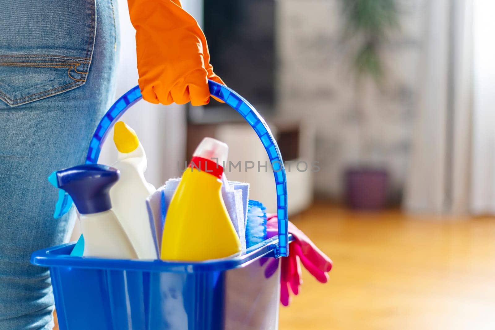 Woman in rubber gloves with bucket of cleaning supplies ready to clean up her apartment. Housewife has many household chores, domestic work and professional cleaning service. Low depth of field