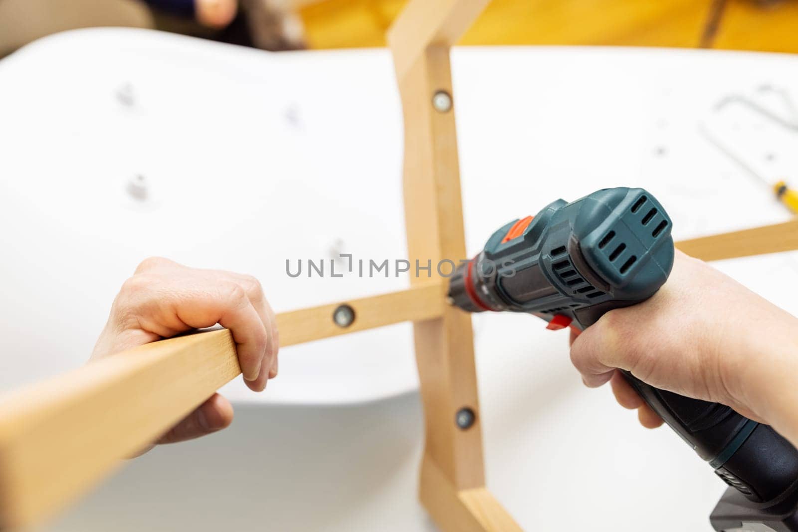 Craftsman collecting and repairing with tools, assembling furniture with drill. Man screws details to chair with electric screwdriver at home after renovation