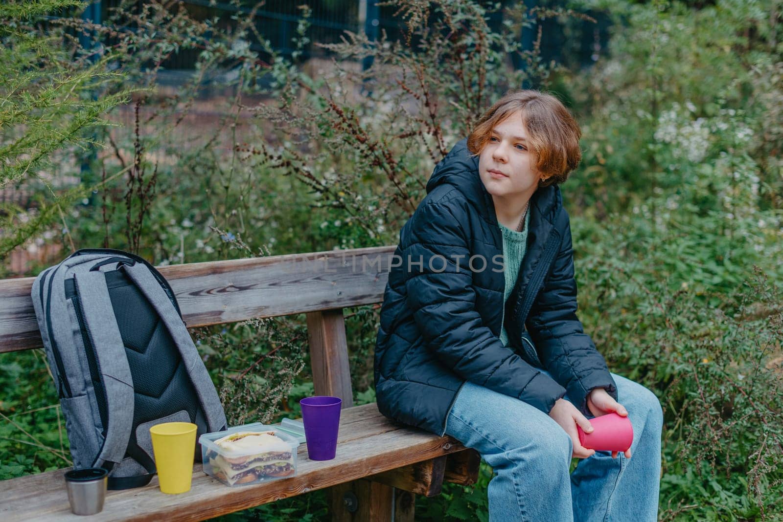 Blonde girl holding cup sitting on bench in the park. Autumn season. Young Teen Girl relaxing on bench with cup of coffee or tea.