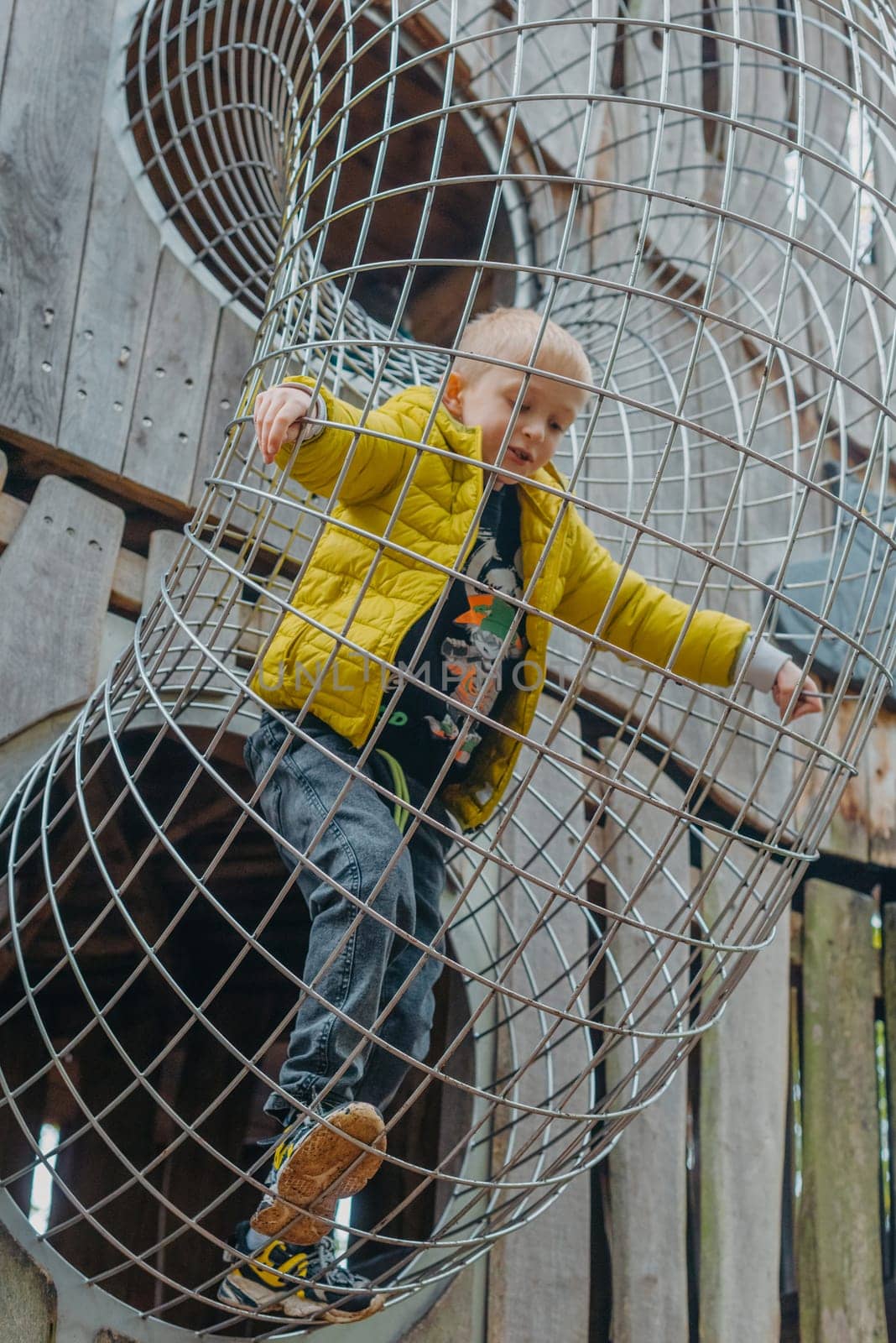 A child climbs up an alpine grid in a park on a playground on a hot summer day. children's playground in a public park, entertainment and recreation for children, mountaineering training. Child playing on outdoor playground. Kids play on school or kindergarten yard. Active kid on colorful slide and swing. Healthy summer activity for children. Little boy climbing outdoors. by Andrii_Ko