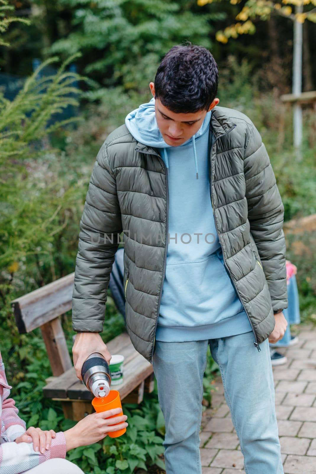 Happy Family drinking tea from a thermos in the forest. Photo of cute charming mother with childrens dressed casual outfit walking sitting bench drinking tea smiling outside city park