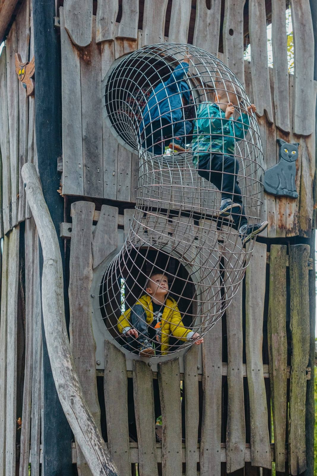 A child climbs up an alpine grid in a park on a playground on a hot summer day. children's playground in a public park, entertainment and recreation for children, mountaineering training. Child playing on outdoor playground. Kids play on school or kindergarten yard. Active kid on colorful slide and swing. Healthy summer activity for children. Little boy climbing outdoors.