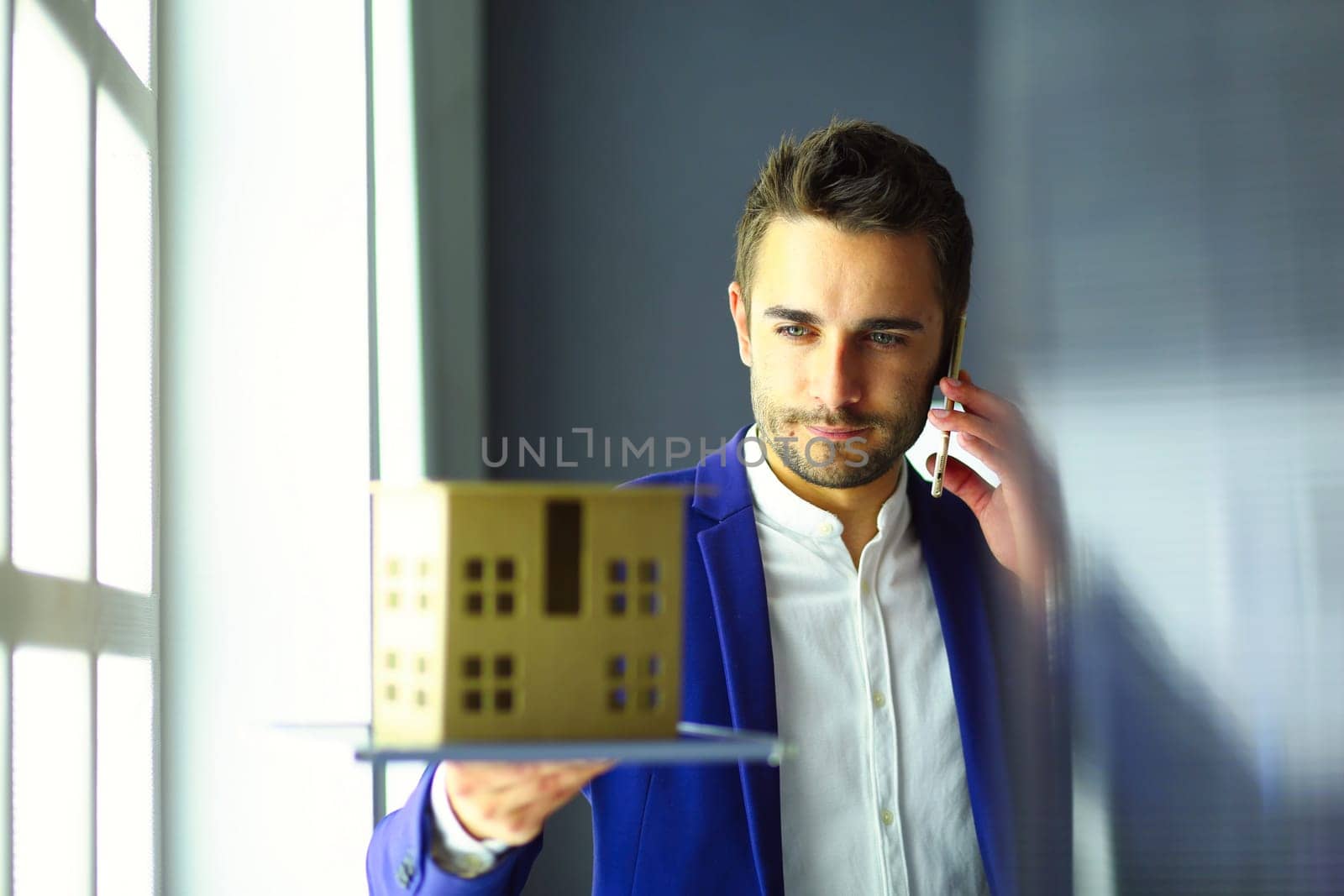 Businessman holding house miniature on hand standing in office. by lenets
