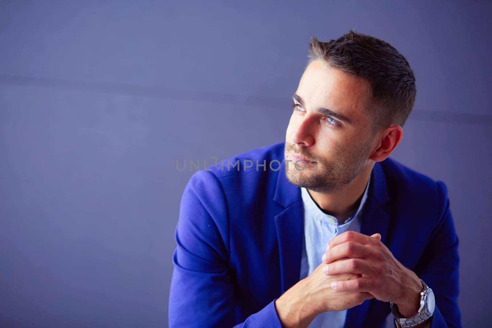 Young businessman sitting isolated on grey background