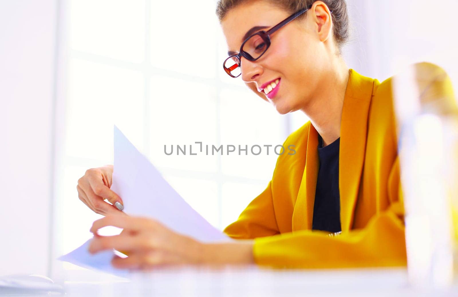 Beautiful young businesswoman doing some paperwork while sitting at office desk in front of laptop