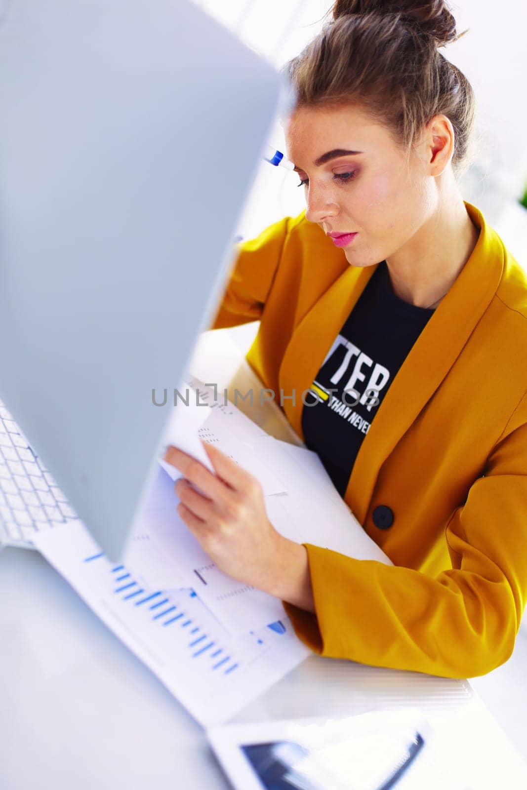 Beautiful young businesswoman doing some paperwork while sitting at office desk in front of laptop