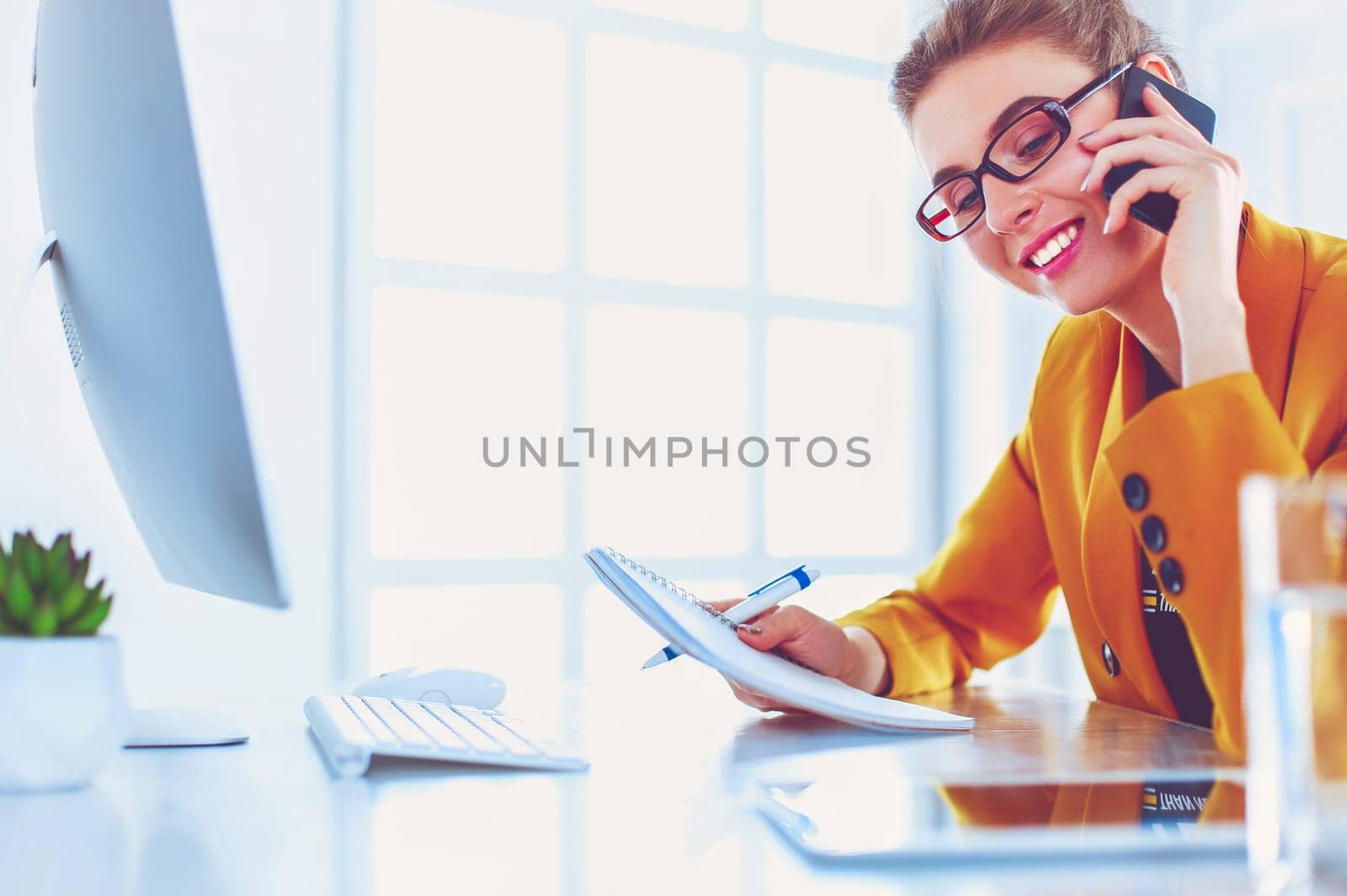 Portrait of beautiful woman making call while sitting at her workplace in front of laptop and working on new project