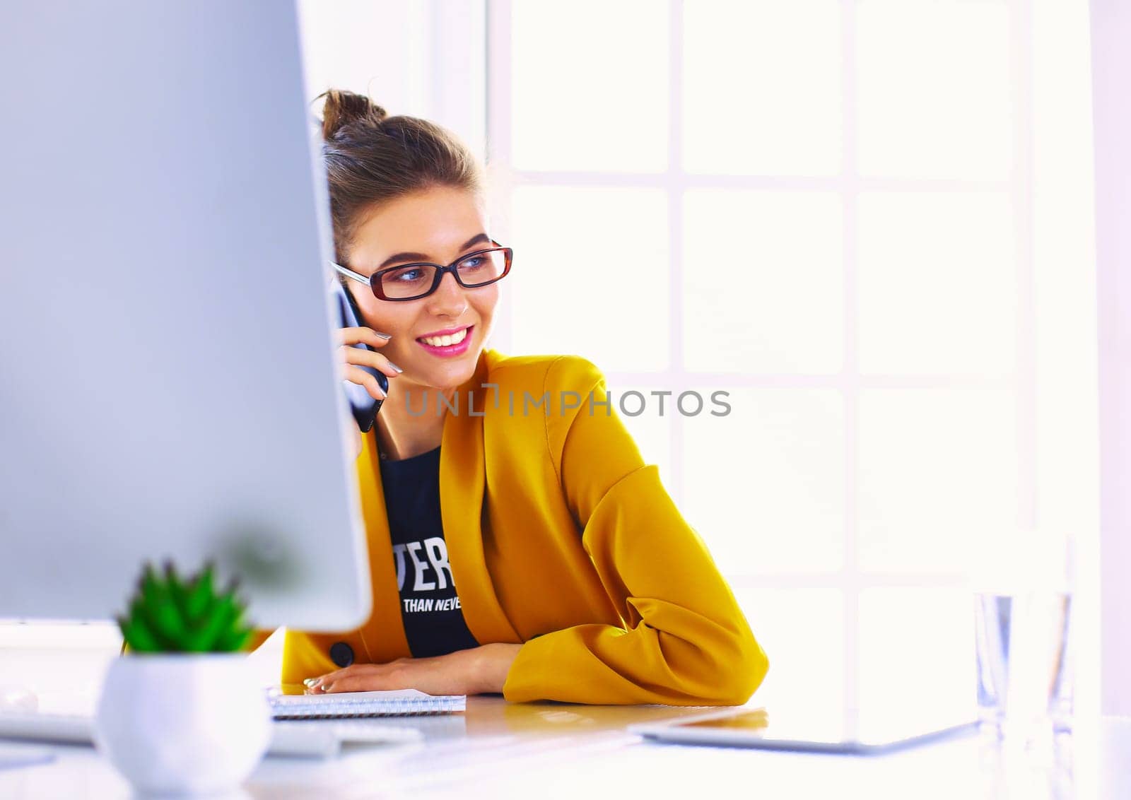 Businesswoman sitting in office with laptop on telephone.
