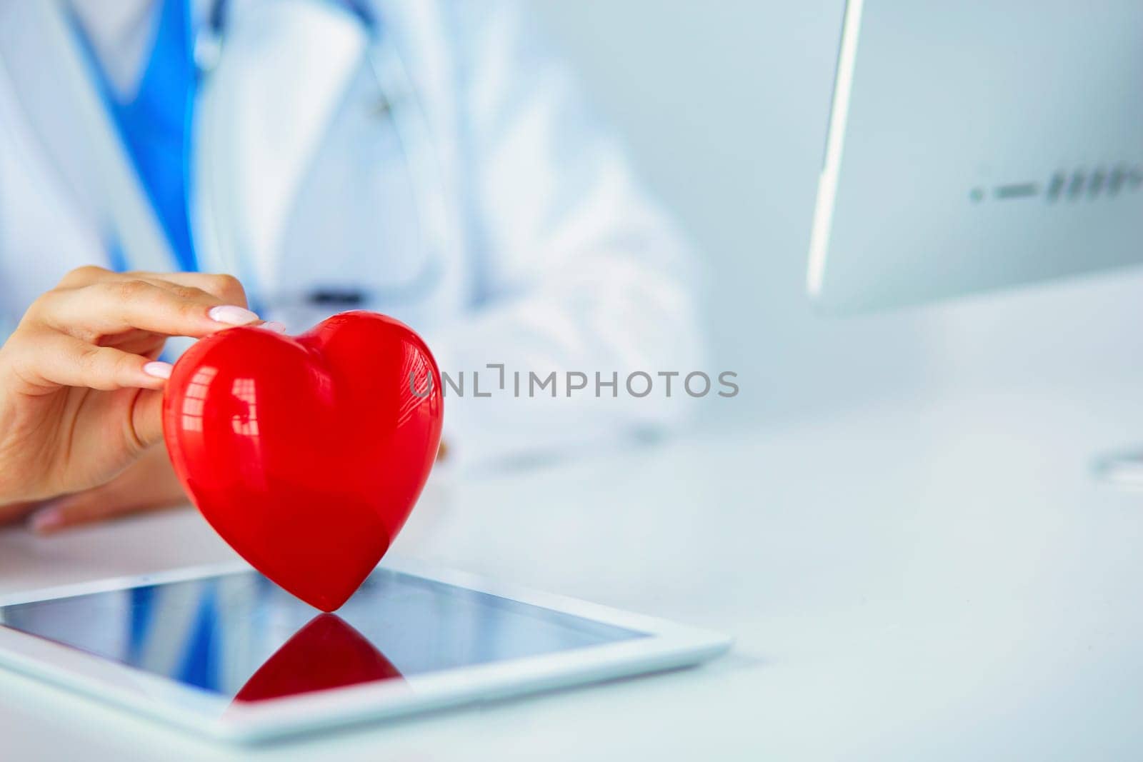 Female doctor with stethoscope holding heart, on light background.